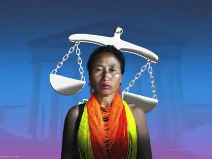 Portrait of a woman standing against a blue-to-purple gradient background with a faint image of a classical courthouse-style building with columns behind her. A large silver balance scale appears above and behind her head, with one side tilted lower than the other. She is wearing a black top and layered beaded necklaces in bright orange, yellow and red. She faces the camera with a serious expression.