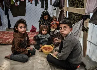 A family is seen sitting around a bowl of beans in their tent in Rafah, in the south of the Gaza Strip. 