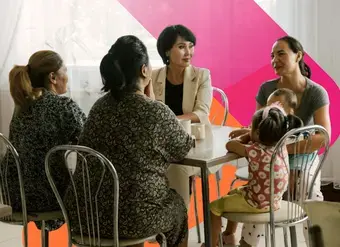 Four women sit and talk around a table. One woman holds a small child in her arms.