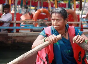 A woman, wearing an official tourist guide vest, steers a boat