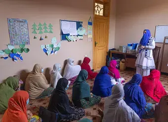 Afghan women sit on a classroom floor and listen closely to a teacher