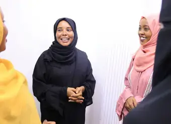 Four young women stand together, talking and laughing