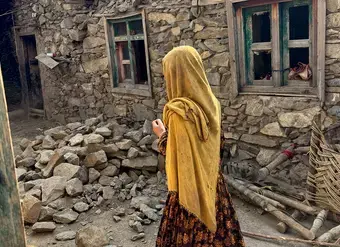 A young woman walks among the stone rubble of a house