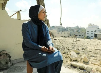  A woman sits amid the ruins of a building.