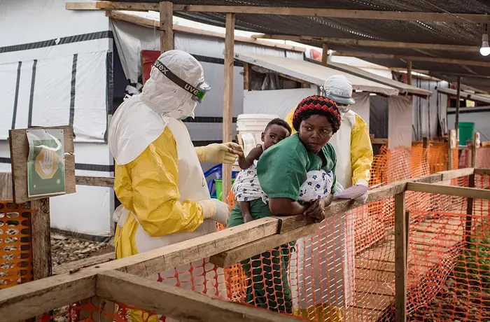 Un professionnel de santé portant un équipement de protection examine un enfant porté sur le dos par une personne qui s'occupe de lui, dans un centre de traitement d'Ebola.