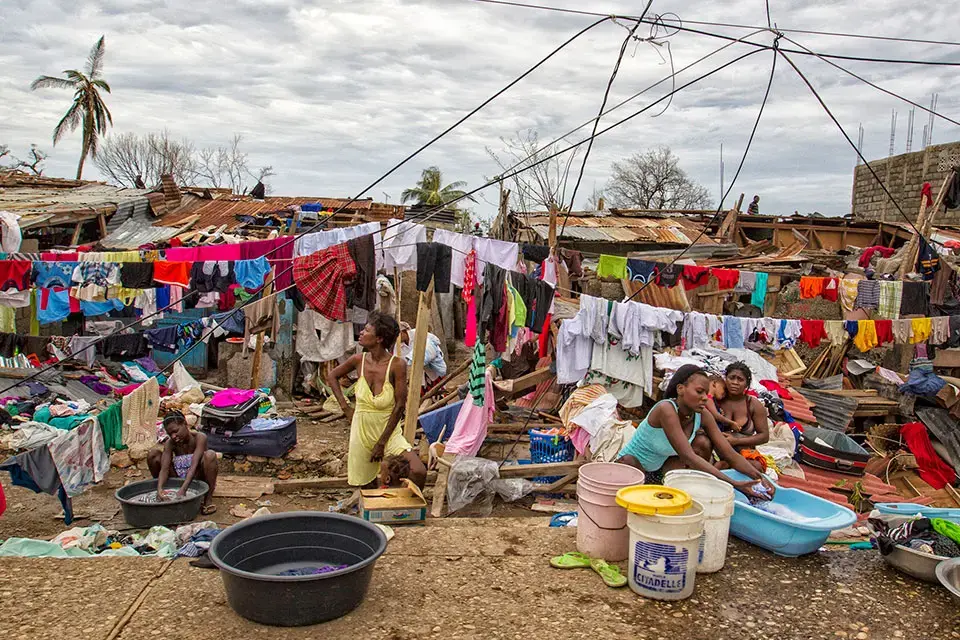 Women and girls wash clothes and care for children amid homes destroyed by Hurricane Matthew.