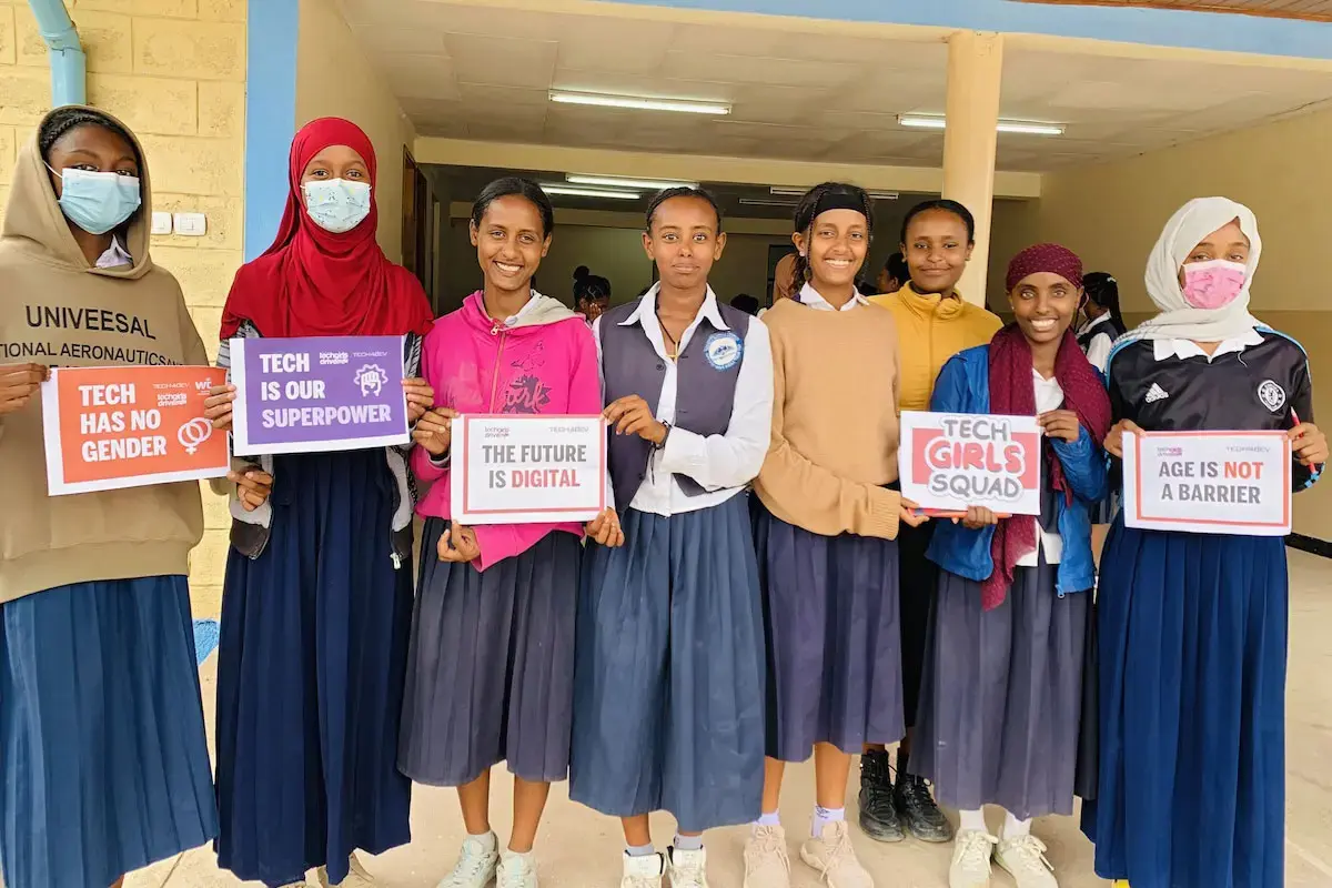 A group of Ethiopian students pose with signs that read "tech has no gender" and "tech is our superpower."