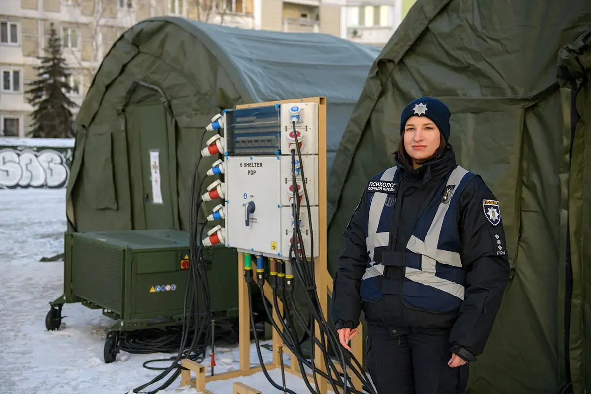 A uniformed woman stands in front of a Ukrainian State Emergency Service tent