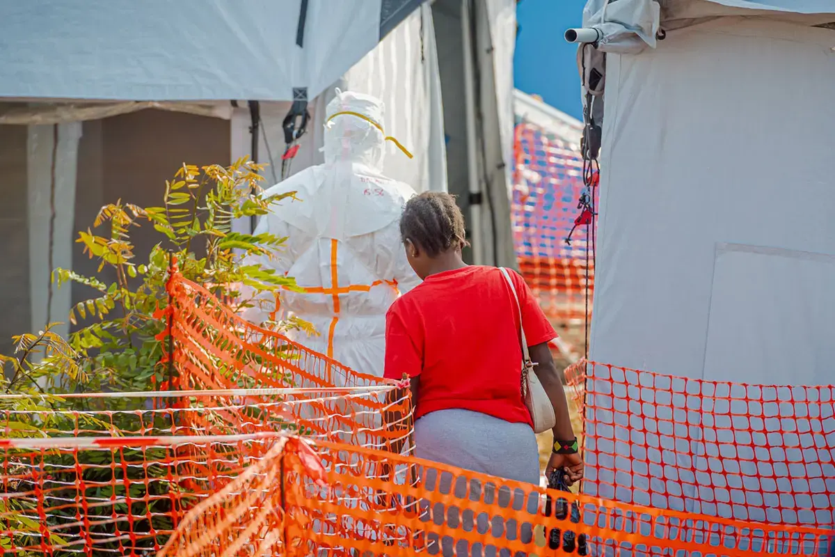 Un professionnel de santé portant un équipement de protection se tient près d'une personne qui emprunte un chemin balisé au sein d'un centre de traitement d'Ebola.