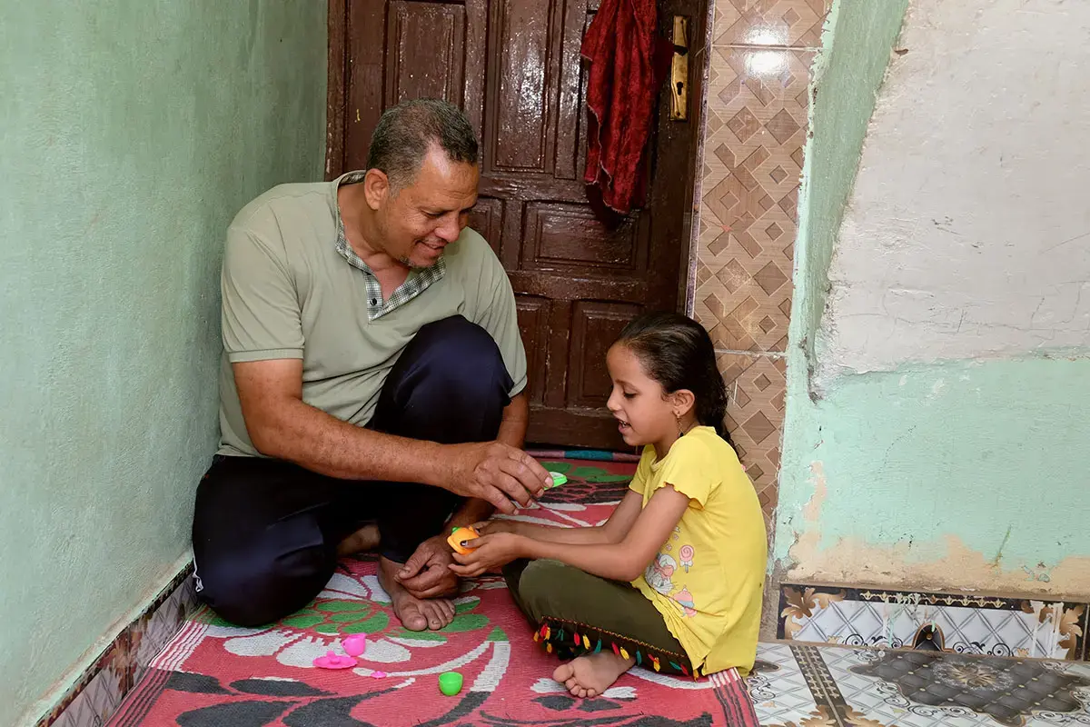 Father and daughter sit on the floor playing together with toys.