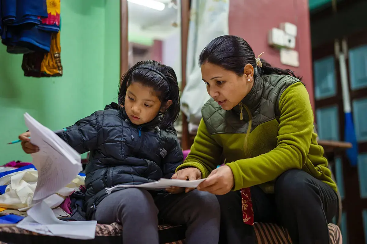 From cooking, cleaning, farming, looking after children and elderly people, and countless more tasks, women carried out 85 per cent of daily unpaid care work in Nepal – almost six times more than men. Photographed here, a woman helps review a child's schoolwork. Photo: UN Women/Srijana Bhatta