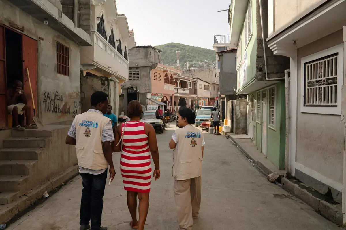A woman walks along a residential street with two UN Women staff members.