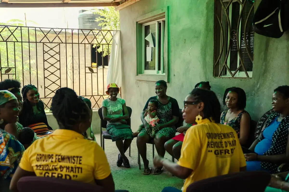 A group of women sit together in a circle during a community meeting.