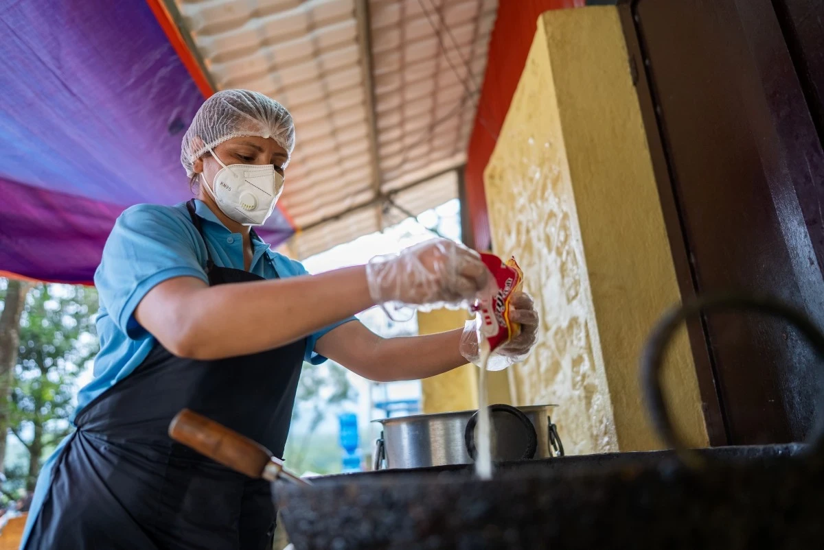 A woman, wearing food-safe attire, pours ingredients into a pot