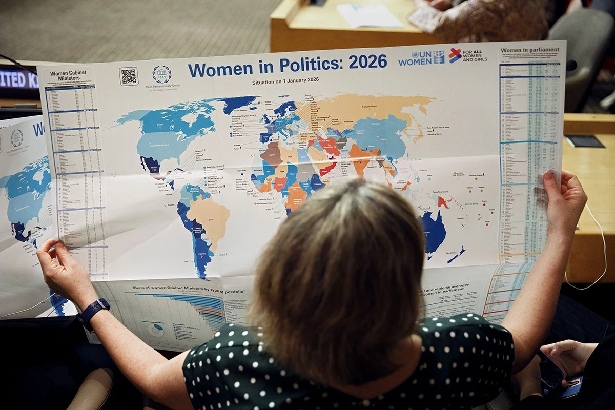 A woman stands over a world map featuring information on women in politics