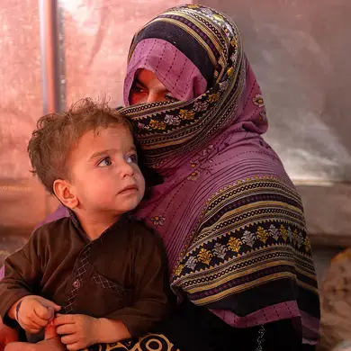 An Afghan woman, who returned from Pakistan earlier that day, rests with her son inside a tent erected to give returnees some shade from the burning sun at Takhta Pul, near the Pakistan border. UN Women: Sayed Habib Bidell.