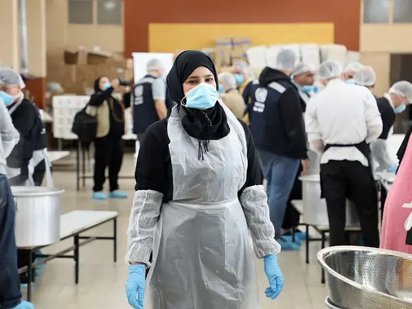 A woman wearing an apron and gloves stands in a community kitchen