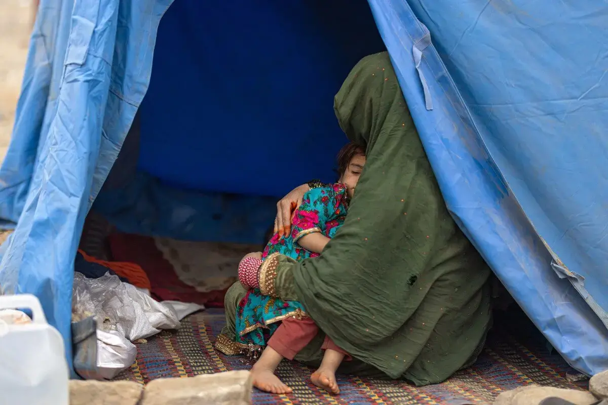 Au poste frontière de Torkham, entre l’Afghanistan et le Pakistan, une femme berce un enfant dans l’ouverture d’un abri de fortune. Novembre 2023. Photo : ONU Femmes / Sayed Habib Bidell.