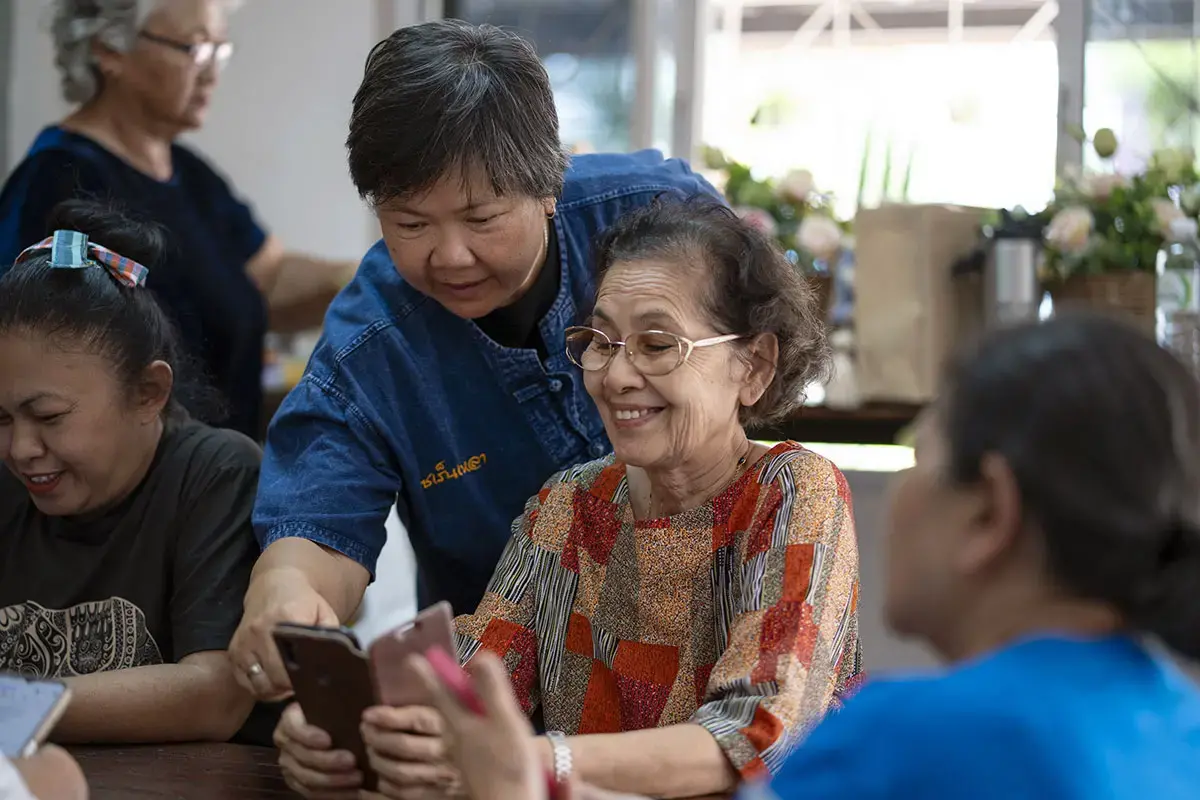 In a cheerful session, Sommas offers friendly guidance to an elder on how torecognize scams and avoid harmful pop-up links on a smartphone. 16 March2025, Muang District, Surin Province.