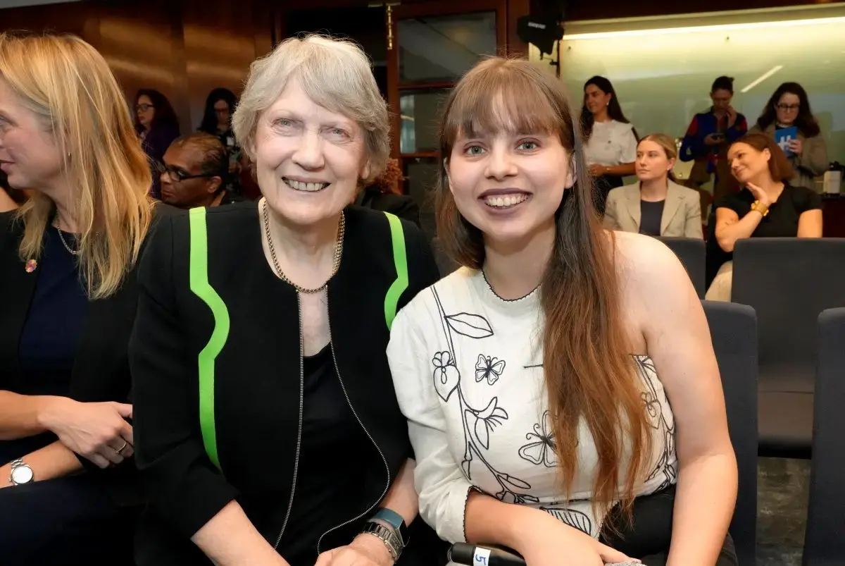 Two women post for a photo together, while one holds a microphone