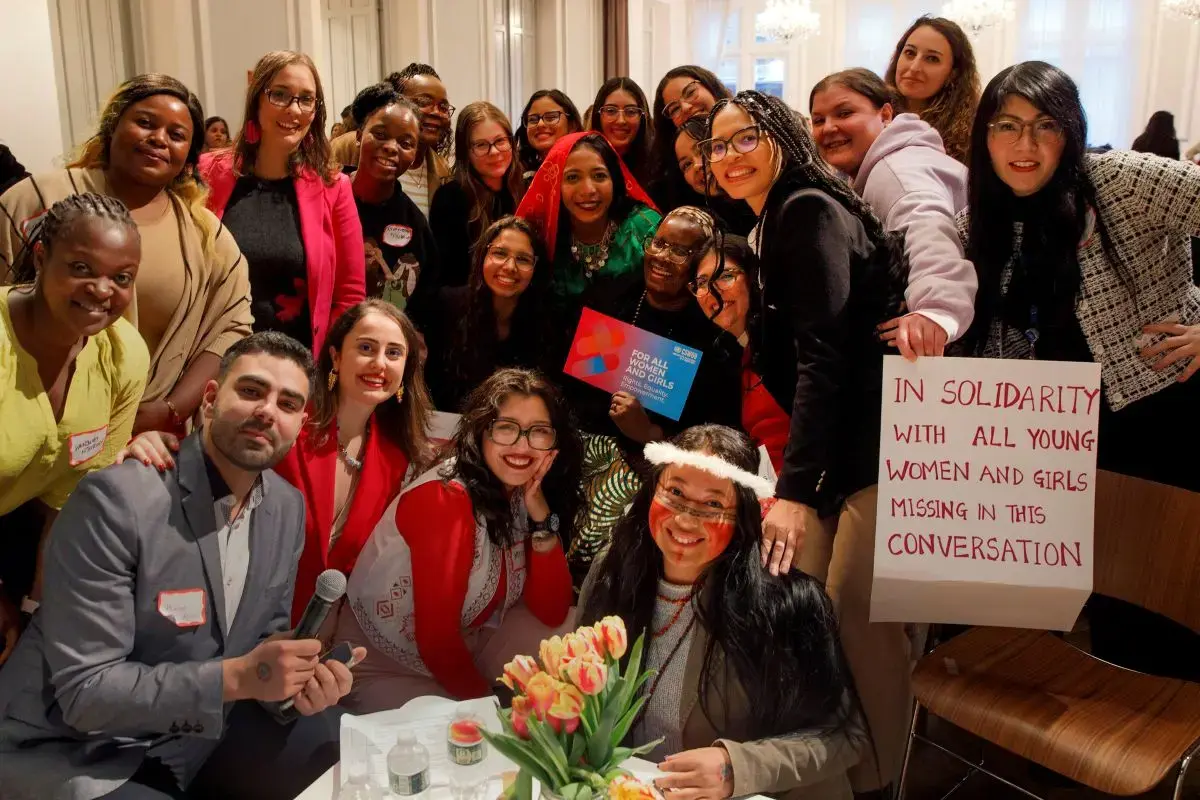 A group of young women pose together with a sign that reads "in solidarity with the women and girls missing from this conversation"