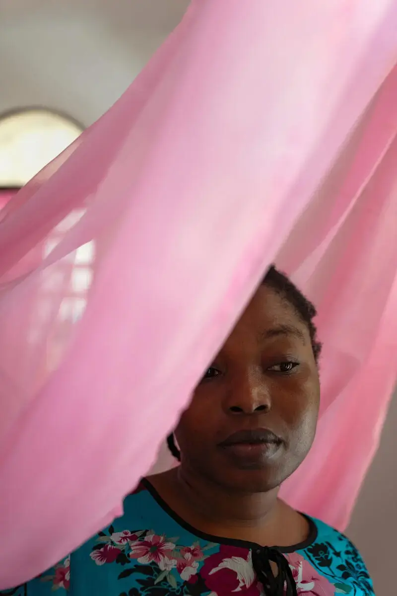 A woman looks through sheer pink fabric draped around her.